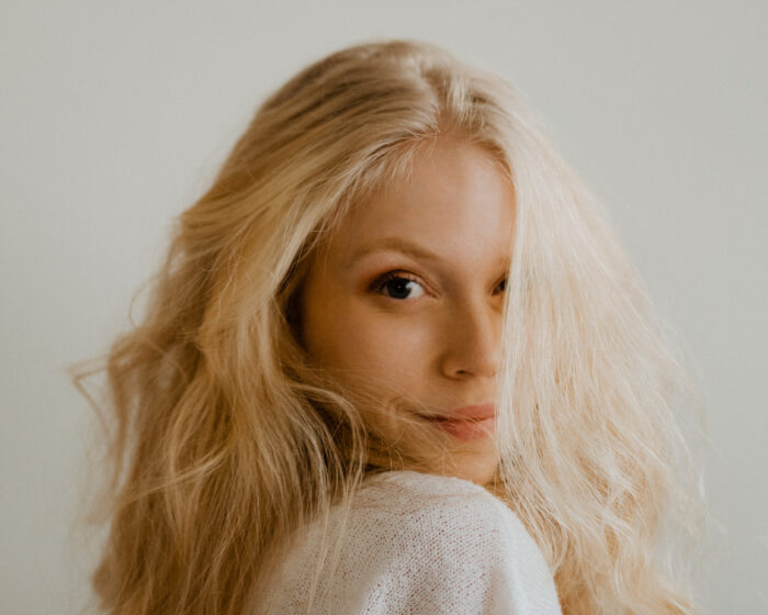 Profile picture of Linda Thörn. Young woman, entrepreneur and photographer with blonde, wavy hair and natural make up, wearing a white knitted sweater.
